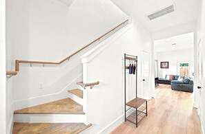 A staircase with wooden steps and a metal handrail, leading to a room with a black metal rack and a sofa.