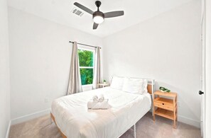 A bedroom with a bed, a nightstand, a ceiling fan, and a window with curtains.