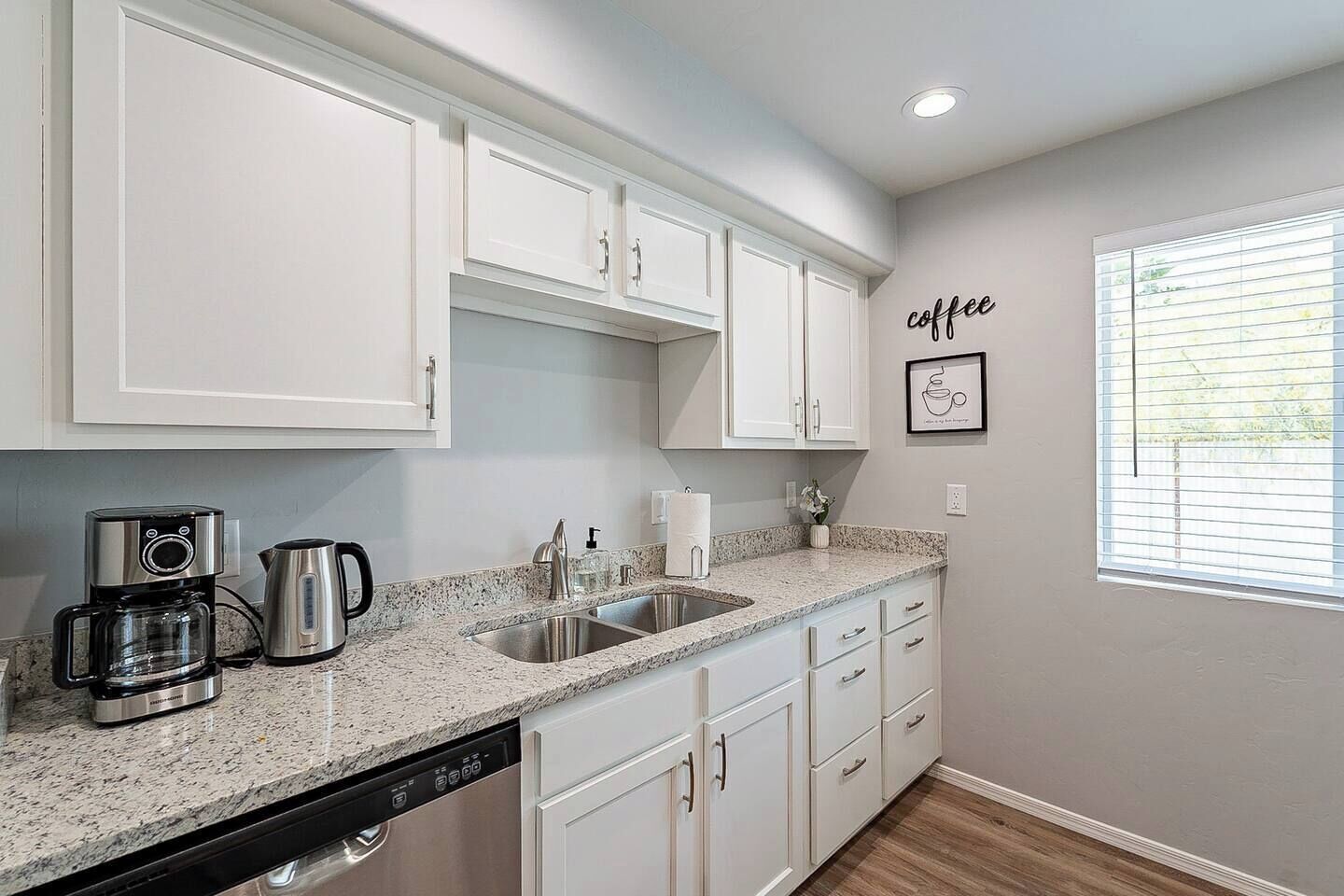 A kitchen with white cabinets, a coffee maker, a kettle, and a sink.