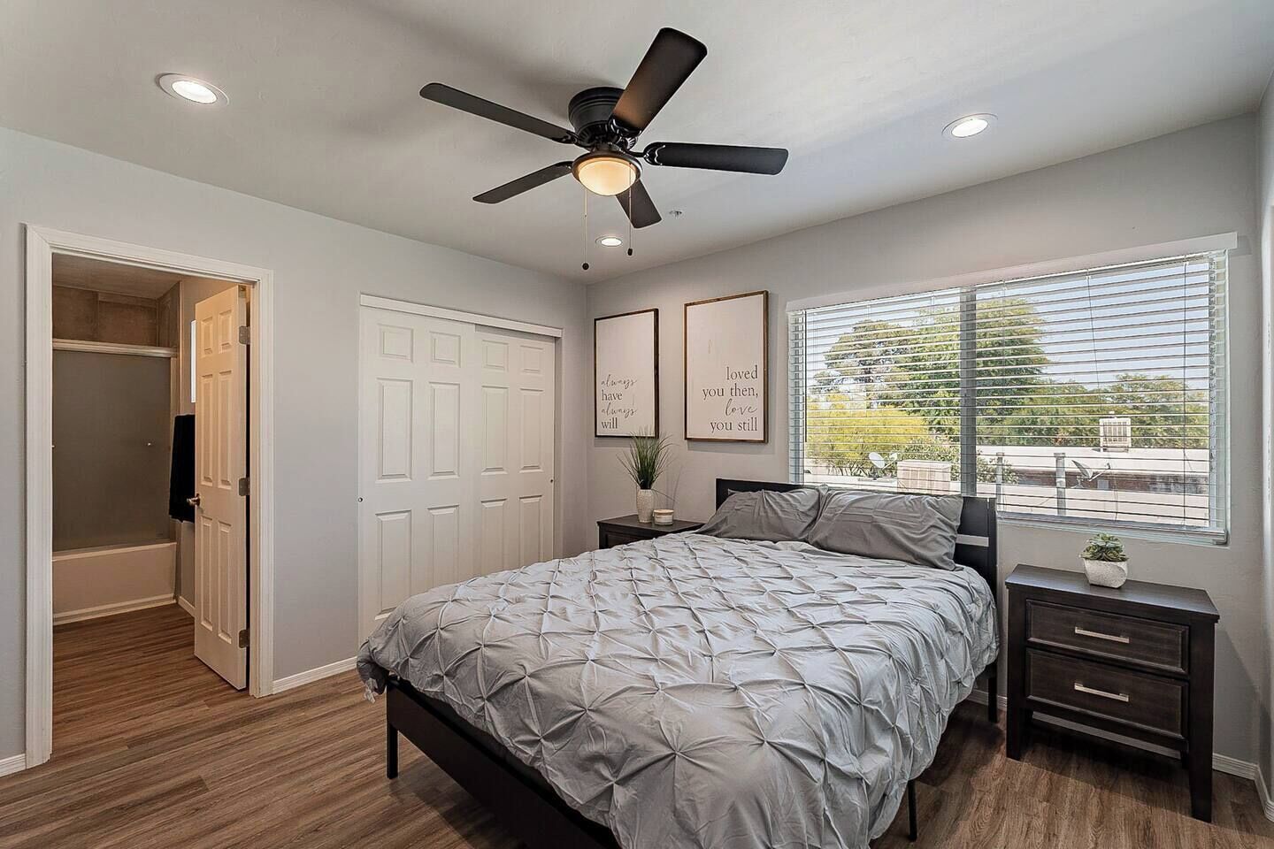 A bedroom with a bed, a ceiling fan, a window with blinds, and a door leading to a closet.