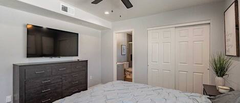 A bedroom with a bed, a dresser, a ceiling fan, a TV, and a closet.