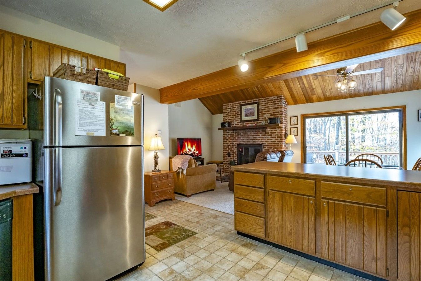 A kitchen with a built-in refrigerator, wooden cabinets, a fireplace, and a large window.