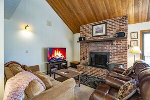 A cozy living room with a brick fireplace, leather sofas, a television, and a wooden ceiling.