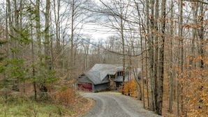 A rural road leading to a stone house with a red garage door, surrounded by trees and a gravel path.