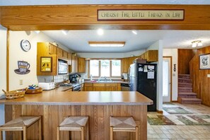 A kitchen with wooden cabinets, a central island with stools, a clock, and a sign above the island.