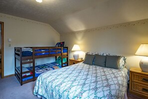 A bedroom with a bunk bed, a single bed, two bedside lamps, and a floral-patterned bedspread.