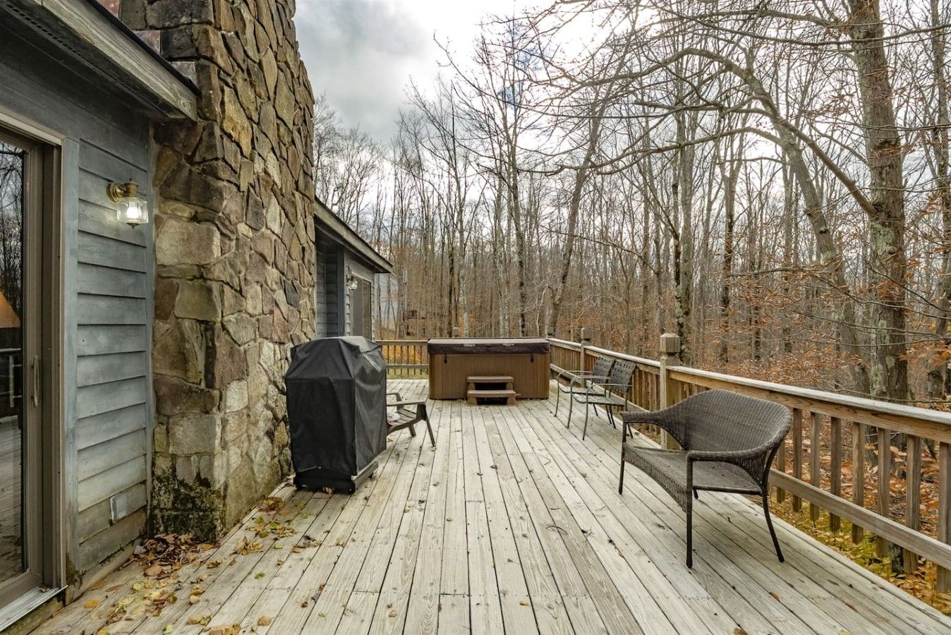 A wooden deck with a stone wall, outdoor seating, and a hot tub.