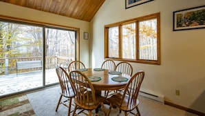 A dining area with a wooden table and chairs, large windows with a view of trees, and a ceiling fan.