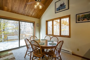 A dining area with a wooden table and chairs, large windows with a view of trees, and a ceiling fan.