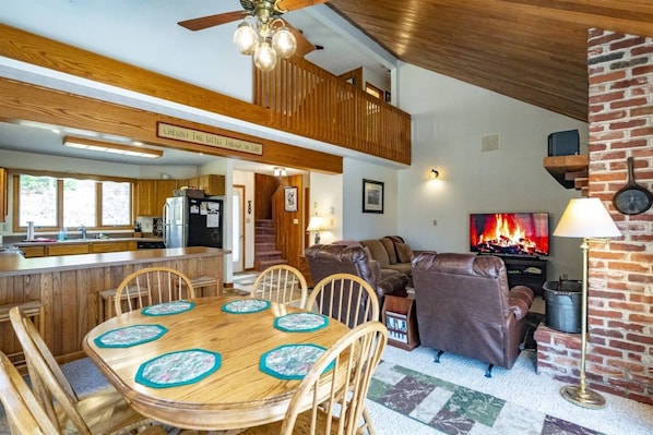 Un espacio habitable amplio con chimenea, una mesa de comedor con sillas y una cocina al fondo.