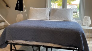 A bedroom with a bed, a window, a staircase, and a bag hanging on a rack. - Cozy, peaceful family-friendly neighborhood-steps away from the credit river (Mississauga)