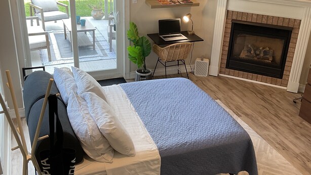 A bedroom with a bed, a desk with a laptop, a fireplace, and a view of the outdoors. - Cozy, peaceful family-friendly neighborhood-steps away from the credit river (Mississauga)