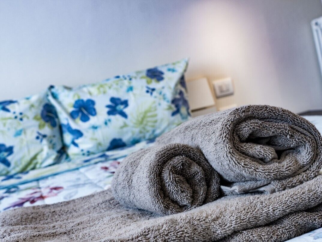 Una cama bien hecha con un cojín estampado con motivos florales y una manta enrollada.