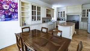 A spacious kitchen with white cabinetry, a wooden dining table, and a painting on the wall.