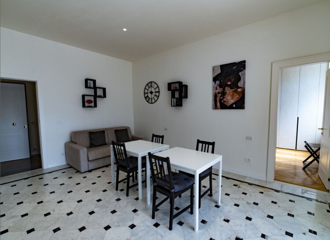 Un coin repas avec une table et des chaises blanches, un canapé et une horloge au mur.