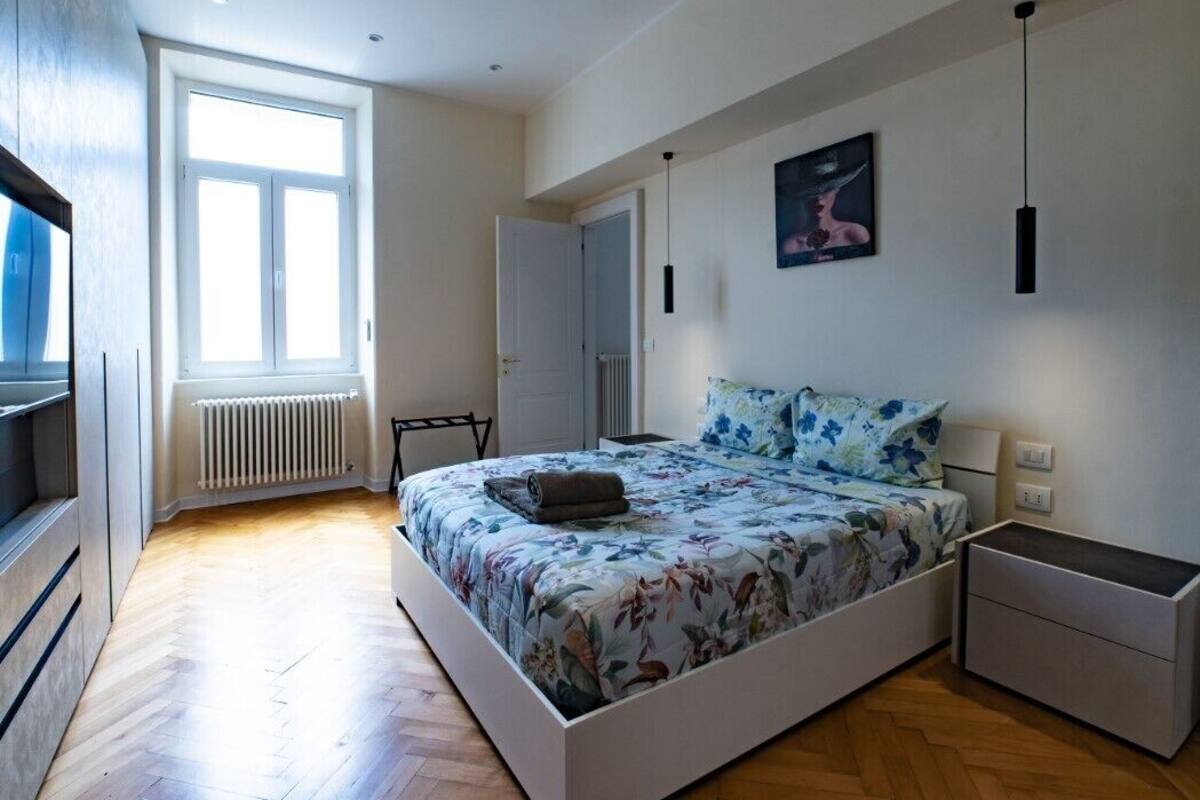 A bedroom with a large bed, a radiator, a window, and a TV.