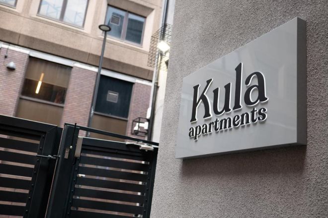 En skylt för ”Kula Apartments” med en modern design, monterad på en vägg med en tydlig struktur.