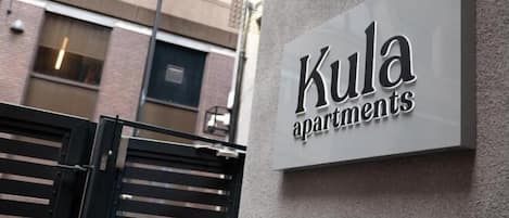 A sign for 'Kula Apartments' with a modern design, mounted on a textured wall.