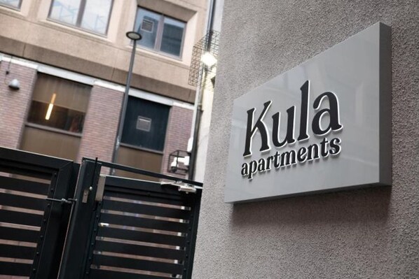 A sign for 'Kula Apartments' with a modern design, mounted on a textured wall. - Kula Manchester (MANCHESTER)