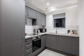 Een moderne keuken met grijze kastjes, een inbouwoven en een raam boven de spoelbak.