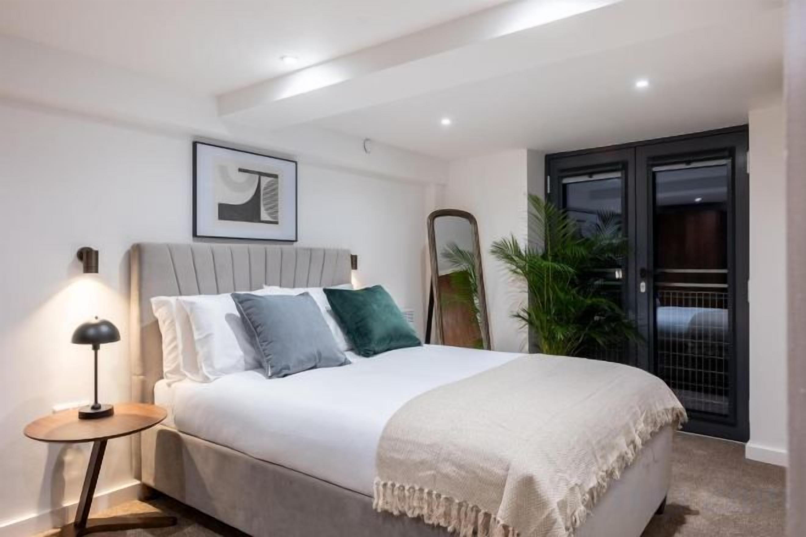 Un dormitorio con cama, mesita de noche, lámpara y puerta que da a un balcón.