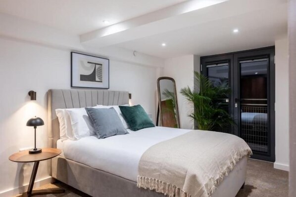 Een slaapkamer met een bed, nachtkastje, lamp en een deur naar een balkon.