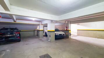 Uma garagem de estacionamento com dois carros estacionados, pilares de concreto e um extintor de incêndio na parede.