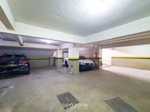 A parking garage with two cars parked, concrete pillars, and a fire extinguisher on the wall. - Modern Apartments 900 m From Beira-mar Norte - EOX (Florianópolis)