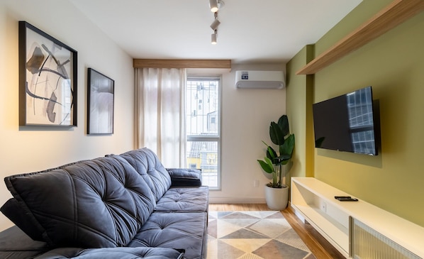 A modern living room with a black leather sofa, a mounted TV, and a large window with curtains.