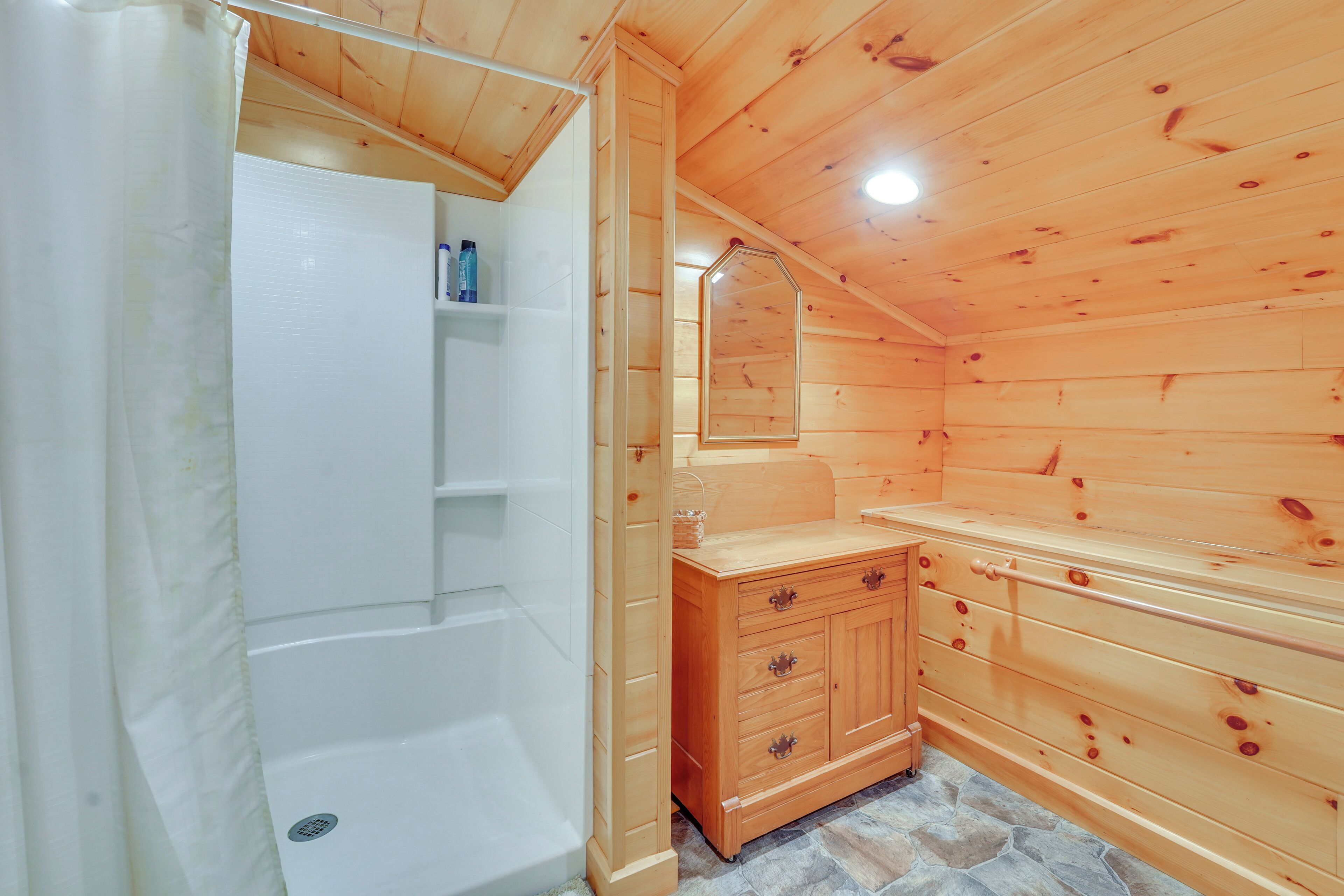 Ein Badezimmer einer Holzhütte mit Dusche, Waschtisch mit Schubladen und Spiegel.