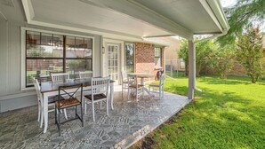 Un patio techado con una mesa y sillas, un muro de ladrillo y un jardín cubierto de césped.