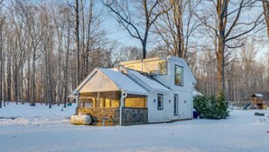 A snow-covered house with a stone foundation, a wooden deck, and a small tree in the yard. - Pet-Friendly Cottage, 2 Mi to Saugatuck Falls (Redding)