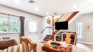 A living room with a wooden chair, a table with books and a box, a television, and a staircase. - Pet-Friendly Cottage, 2 Mi to Saugatuck Falls (Redding)
