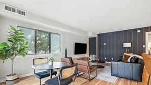 Ein modernes Wohnzimmer mit Essbereich, einer Couch, einem Fernseher und einem großen Fenster.