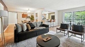 Ein modernes Wohnzimmer mit einem schwarzen Ledersofa, einem runden Couchtisch und einem Essbereich, mit einer Küche im Hintergrund.