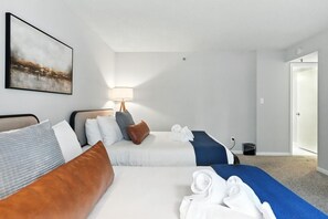 Habitación de hotel con dos camas, una lámpara de noche, un cuadro en la pared y una puerta que da a otra habitación.