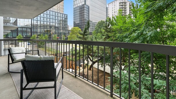 Ein Balkon mit Gartenmöbeln, Blick auf moderne Gebäude und üppiges Grün.