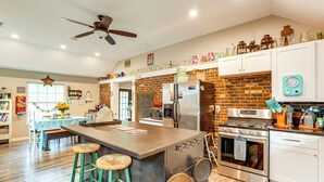 Una cocina amplia con una isla grande, electrodomésticos de acero inoxidable y una pared de ladrillo decorativa.