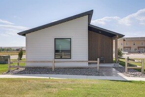A modern single-story building with a sloped roof, a large window, and a wooden deck area. - Mtn-Views, Pet-Friendly! Family Home in Ranchester (Ranchester)