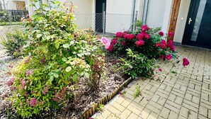 Un edificio residencial con un patio empedrado, una cerca de metal y plantas con flores.