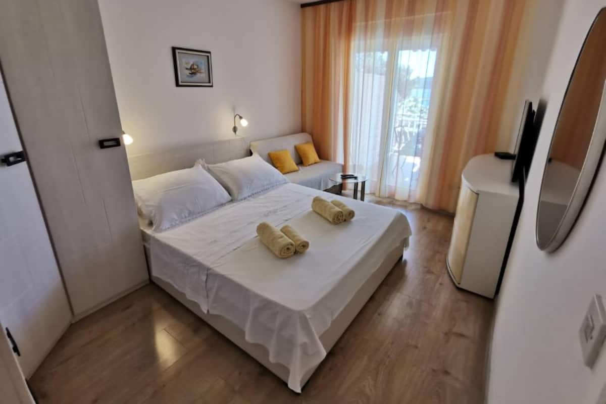 Ein Hotelzimmer mit einem Bett, einem kleinen Tisch, einem Stuhl, einem Fernseher und einem Fenster mit Vorhängen.