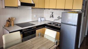 A compact kitchen with yellow cabinets, a stainless steel refrigerator, a built-in oven, and a glass dining table. - Apartments Jaman Dalmatica Čiovo (Okrug)