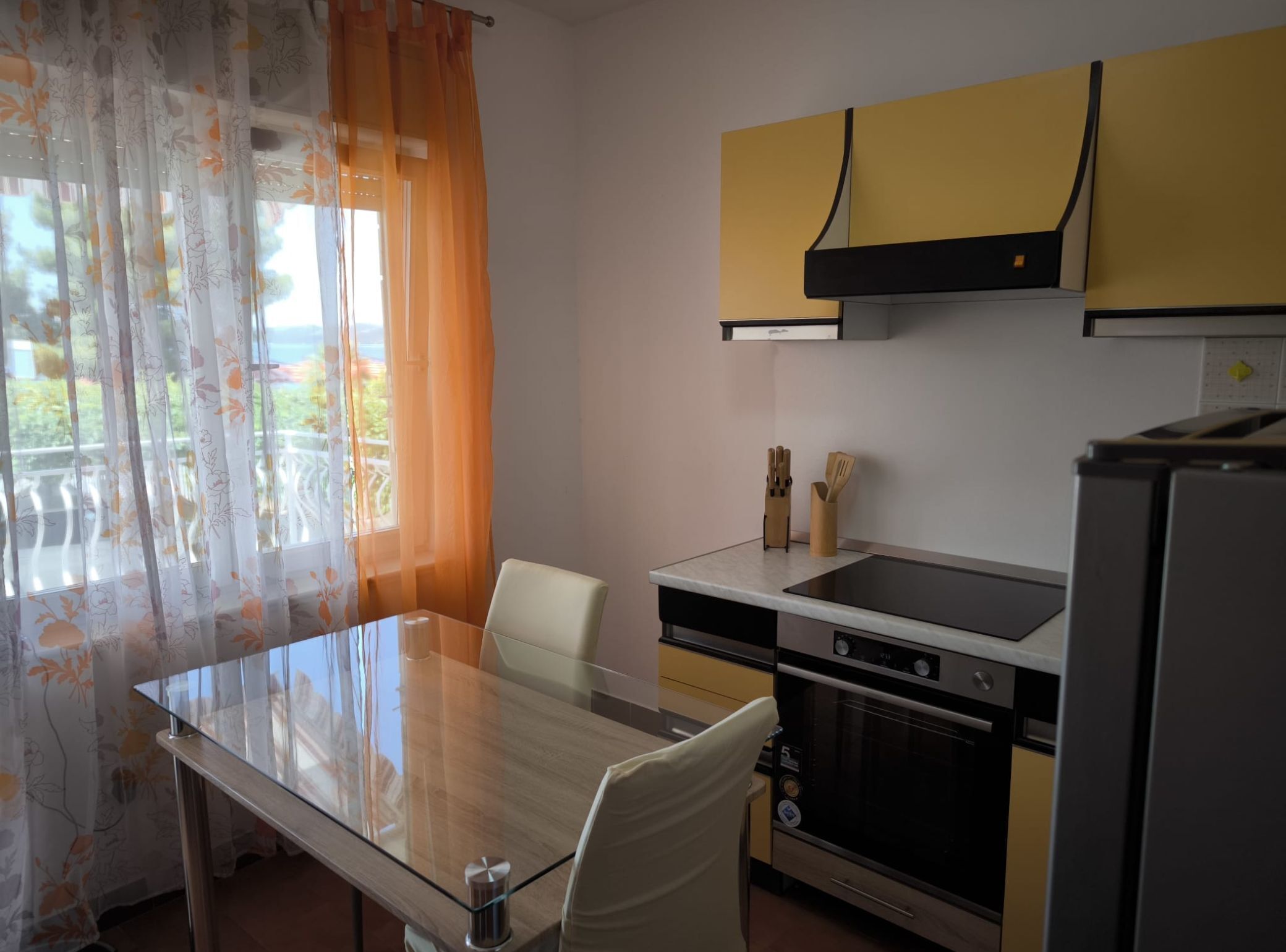 A compact kitchen with a glass dining table, a built-in oven, and a refrigerator.