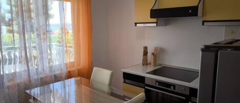 A compact kitchen with a glass dining table, a built-in oven, and a refrigerator.