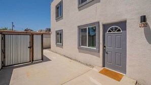 A two-story building with a gray door and windows, a small porch, and a metal gate.