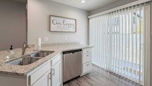 A modern kitchen with granite countertops, stainless steel appliances, and a large window with vertical blinds.