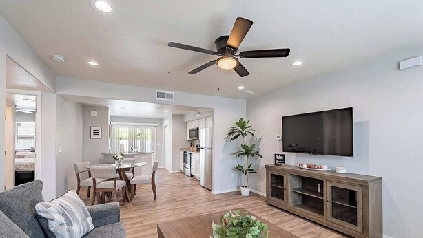 A modern living room with a ceiling fan, a flat-screen TV, a wooden coffee table, and a dining area with a table and chairs.