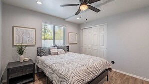 A bedroom with a bed, a nightstand, a ceiling fan, and a window with blinds.
