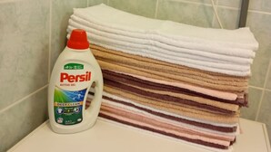 Eine Flasche Persil Active Gel und ein Stapel Handtücher auf einer Badezimmerablage.