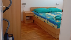 Ein Schlafzimmer mit einem hölzernen Bett, türkisfarbenen Kissen, einem Nachttisch und einem Staubsauger.